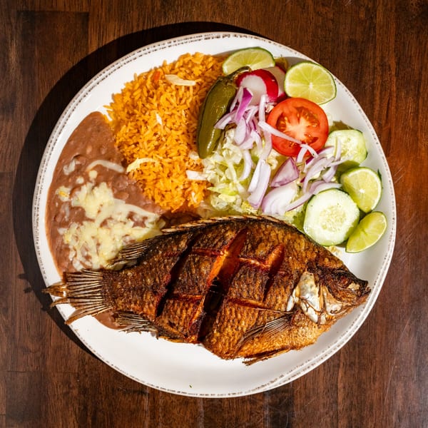 Fried whole fish with rice, refried beans, and a side salad with lime on a white plate.